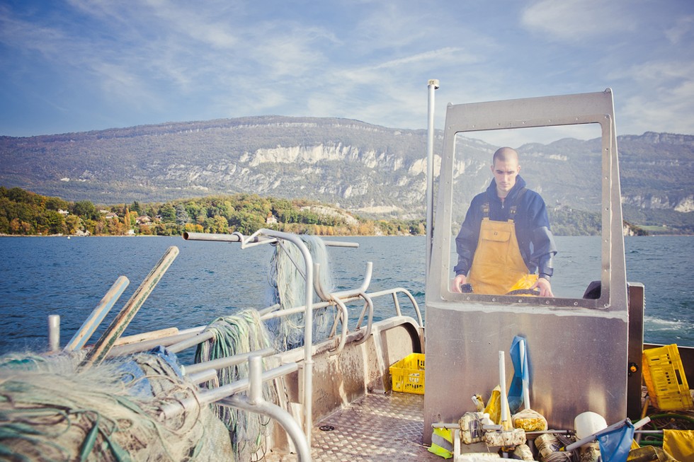 Un pêcheur sur sa barque travaille ses filets sur le lac du Bourget
